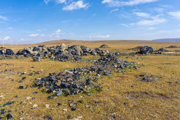 Huge obsidians lie on autumn grass in the sun. Hills and blue sky in the background