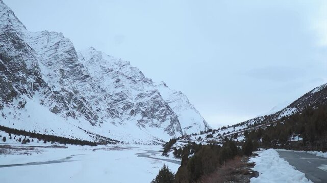 Snowy mountain range with snow and frozen river in Lahaul, Himachal Pradesh, India. Empty asphalt road during winter day.