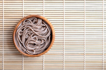 Chilled, boiled soba noodles in a wooden bowl placed on a bamboo mat. Thin Japanese noodles, made primarily from buckwheat flour, with wheat flour mixed in. With empty space for text or other content.