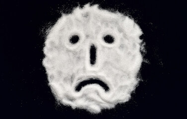 Sad face drawn on the scattered refined white sugar on the black background. Top view. Stop diabetes and healthy diet concept.