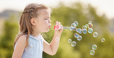 Girl, child and blowing bubbles in garden, playful and outdoor with liquid, toys and sunshine. Kid,...