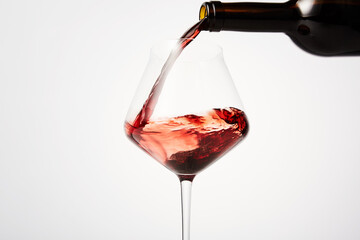 Red wine pouring into tilted wineglass from bottle.