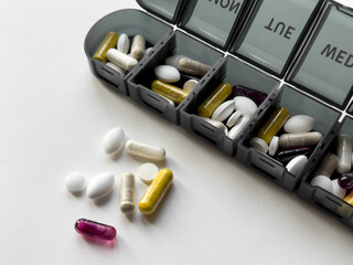 Weekly pill organizer with various tablets and capsules on white surface