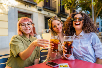 Women toasting to camera enjoying at terrace of a bar