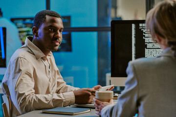 Young African American programmer listening to his female colleague during meeting in cybersecurity department office