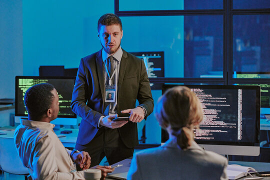 Young Caucasian white-hat hacker speaking during meeting in cybersecurity department office, copy space