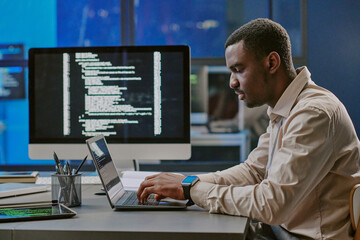 Side view of young Black male white-hat hacker testing security system on laptop in modern...