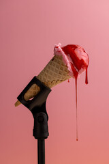 A ball of ice cream in a cone in a microphone stand with dripping drops of berry syrup, the concept of the music industry