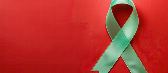 Top view of a light green awareness ribbon on a red background with copy space image available for text