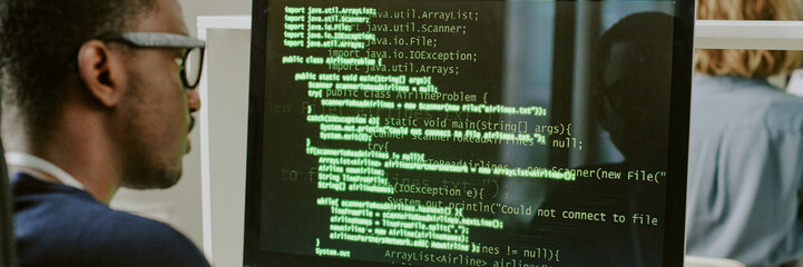 Over shoulder shot of young African American ethical hacker working with code on desktop computer...