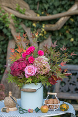 Blumenstrauß mit pink Rosen, Hortensienblüten und Ahornzweigen in einer vintage Milchkanne im Herbst-Garten