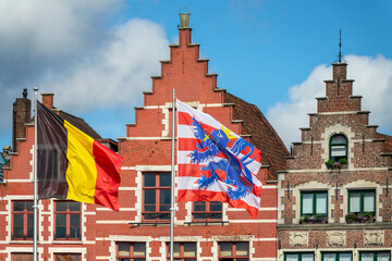 Fototapeta premium Flags of Belgium and of the city of Bruges with colorful houses on Bruges Markt (Market Square), Belgium
