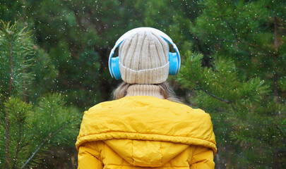 Back view woman enjoying listening to music with headphones in winter forest against Christmas tree