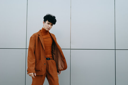 Stylish young man in a brown outfit posing confidently against a minimalist gray wall