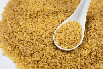 Uncooked bulgur cracked wheat in a spoon close-up