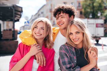 Group of young three stylish friends posing in the street. Fashion man and two cute female dressed in casual summer clothes. Smiling models having fun. Cheerful women and guy outdoors