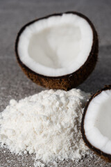 Coconut flour among coconut halves on gray stone background.