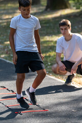 Boy exercises outdoors with a trainer using an agility ladder. The session promotes coordination, speed, and physical fitness in a fun, engaging environment under the guidance of a professional.