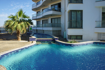 Glistening blue waters reflect the sun as palm trees sway near a stylish modern apartment building