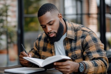 Concentrated man writing in notebook while enjoying coffee break in modern cafe