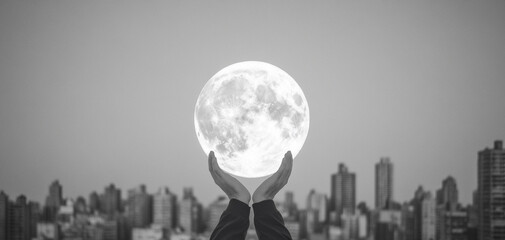 Hands holding a large moon against a city skyline, black and white photography.