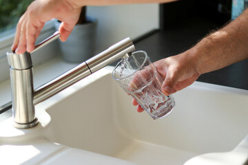 Close up of male hands pouring tap water into a glass in the kitchen