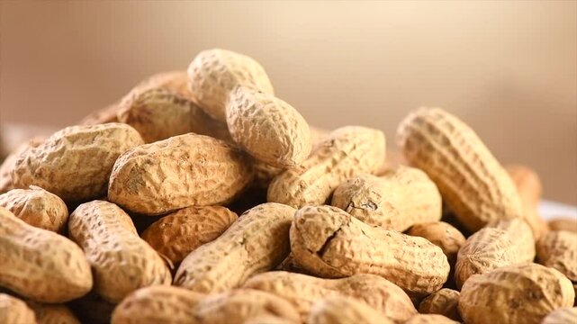 Peanuts. Unshelled nuts close up, rotating. Roasted pile of peanuts in shell over beige background. Organic vegan, vegetarian food. Healthy nutrition concept 