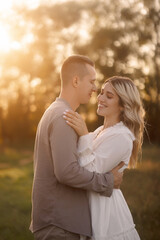 Fototapeta premium Happy young couple in love standing in summer park. Man in gray and girl in white light dress walking.