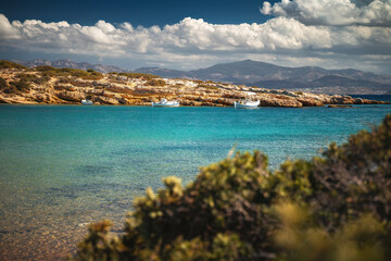 A serene beach on Paros Island, Greece, with golden sands, clear turquoise waters, and gentle waves. Framed by rocky cliffs and lush greenery, it's an idyllic Mediterranean escape under the sun.