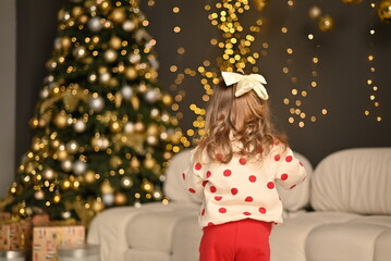 A little girl with a bow in her hair looks for a gift under the Christmas tree.