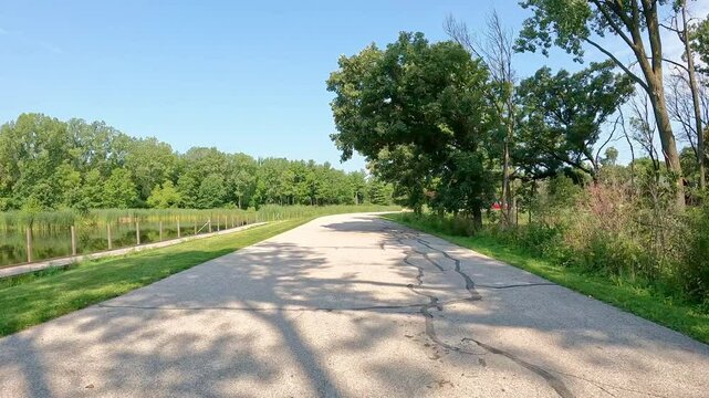 POV - driving on paved road thru Jester County Park in Central Iowa; driving past a pond, parking lot for a trail head, and wooded ares in late summer in the Des Moines River valley; vacation, holiday