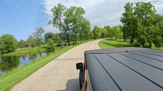 POV from vehicle roof - driving on road thru Jester County Park in Central Iowa; driving past a pond, golf greens, and wooded ares in late summer in the Des Moines River valley; vacation, holiday