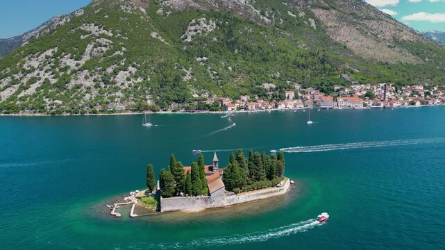 Aerial drone view of Sveti Dorde Island - Saint George Monastry in the middle of the island. In background is Perast city. Famous travel destination in Montenegro. Static footage. Boats passing.