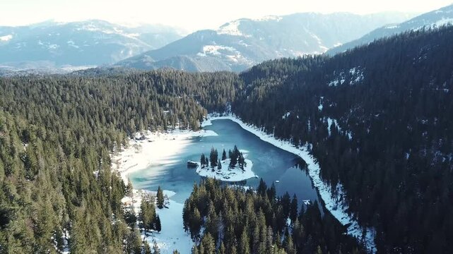 drone pull out shot of Cauma Lake or Caumasee and its small island in the middle,fwith crystal blue frozen water in beautiful mountain landscape scenery at Flims, Graubuenden - Switzerland
