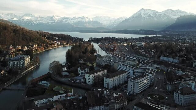 Drone shot revealing the cityscape of Thun in Switzerland, nestled along the Aare river and Thunersee lake, with the majestic swiss alps providing a breathtaking backdrop