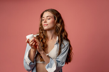studio beauty shoot on pink background long-haired girl posing in underwear and blue shirt with jar...