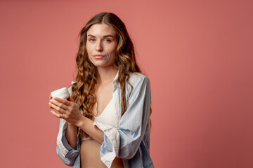 studio beauty shoot on pink background long-haired girl posing in underwear and blue shirt with jar...