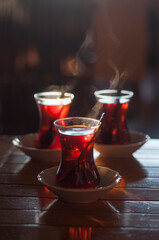 Beautiful backlit photo with shallow depth of field of piping hot Turkish tea served in traditional glasses   on a wooden table