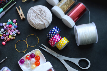 Colorful beads, coloring pencils, glitter, needles, string, hoop, tape and scissors on dark...