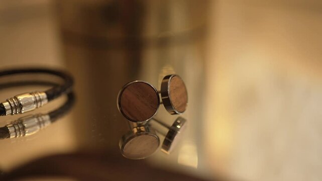 Close up of groom's cufflinks and bracelet reflected on a glass surface with soft lighting