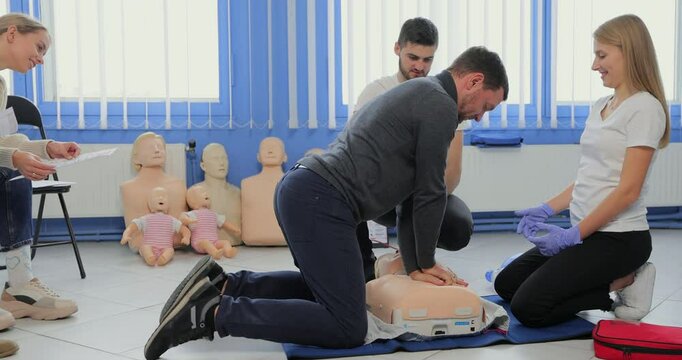 Young woman instructor helping to make first aid heart compressions with dummy during the group training indoors.