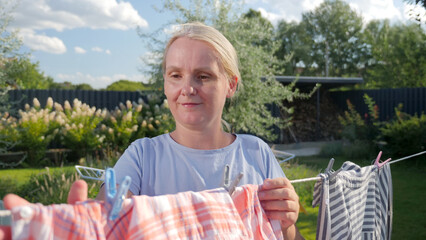 Middle-aged woman hanging laundry on a clothesline outdoors, with a focused expression, in a sunny...