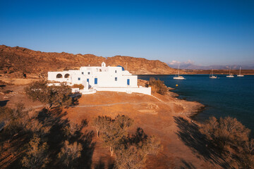 A charming blue-domed chapel on Paros Island, Greece, set against the backdrop of the shimmering Aegean Sea. The whitewashed walls, vibrant dome, and surrounding stone path create a picturesque scene 