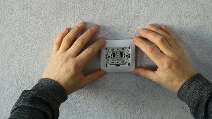 worker fixing or maintaining an electrical outlet or light switch attaching a white plastic frame...
