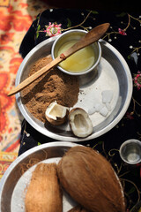 An elaborate setup of traditional Hindu puja items, including coconuts, rose petals, rice, ghee, and sacred offerings, beautifully displayed on an ornate cloth for a religious ceremony.