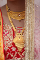 A stunning handcrafted gold necklace with intricate patterns, highlighted by delicate ruby stones, set against a richly embroidered red fabric.