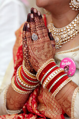 A bride's beautifully decorated hands in a traditional Namaste gesture, adorned with intricate henna designs, red and gold bangles, and elegant jewelry, symbolizing grace and cultural heritage.