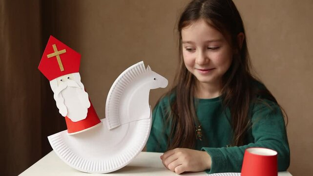 paper craft from paper plates and glasses for kids. DIY toy Saint Nicholas and white horse for sinterklaas day. create art for children. Happy girl with gift