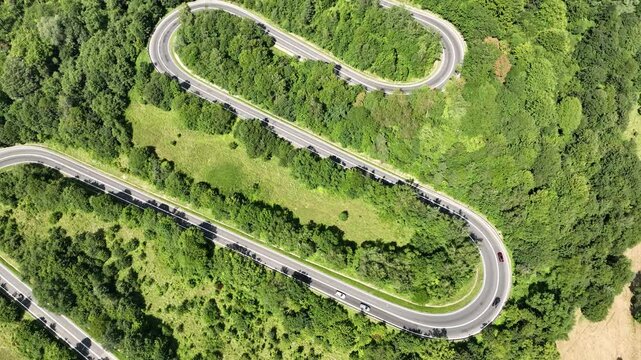 Drone flight in the mountains over a winding road with passing cars surrounded by a dense forest. Mavic 3