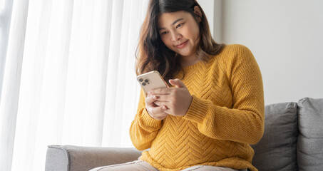 Pregnant asian woman holding smartphone at home using mobile app for pregnant women